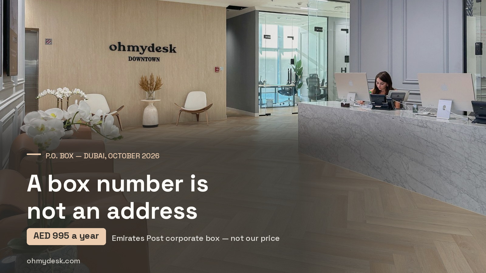 Reception at Oh My Desk Downtown Dubai, with a member of staff at the marble counter, a wood-panelled wall sign and leather armchairs, where members’ mail and parcels are received